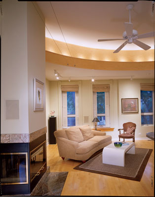 
To help the open, airy living room retain an intimate scale, architect Mark A. Miller continued the curved balcony inside the home, where it becomes a maple soffit with hidden cove lighting. Ray reconstructed the house’s original window shutter boxes that allow shutters to fold into the wall. Illuminated pedestals in the room display some pieces of Ray’s art glass collection.
